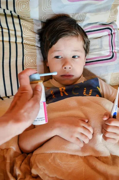 Child with a fever lying in bed while a caregiver checks temperature with a thermometer