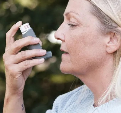Woman using an inhaler to manage breathing difficulty or asthma symptoms